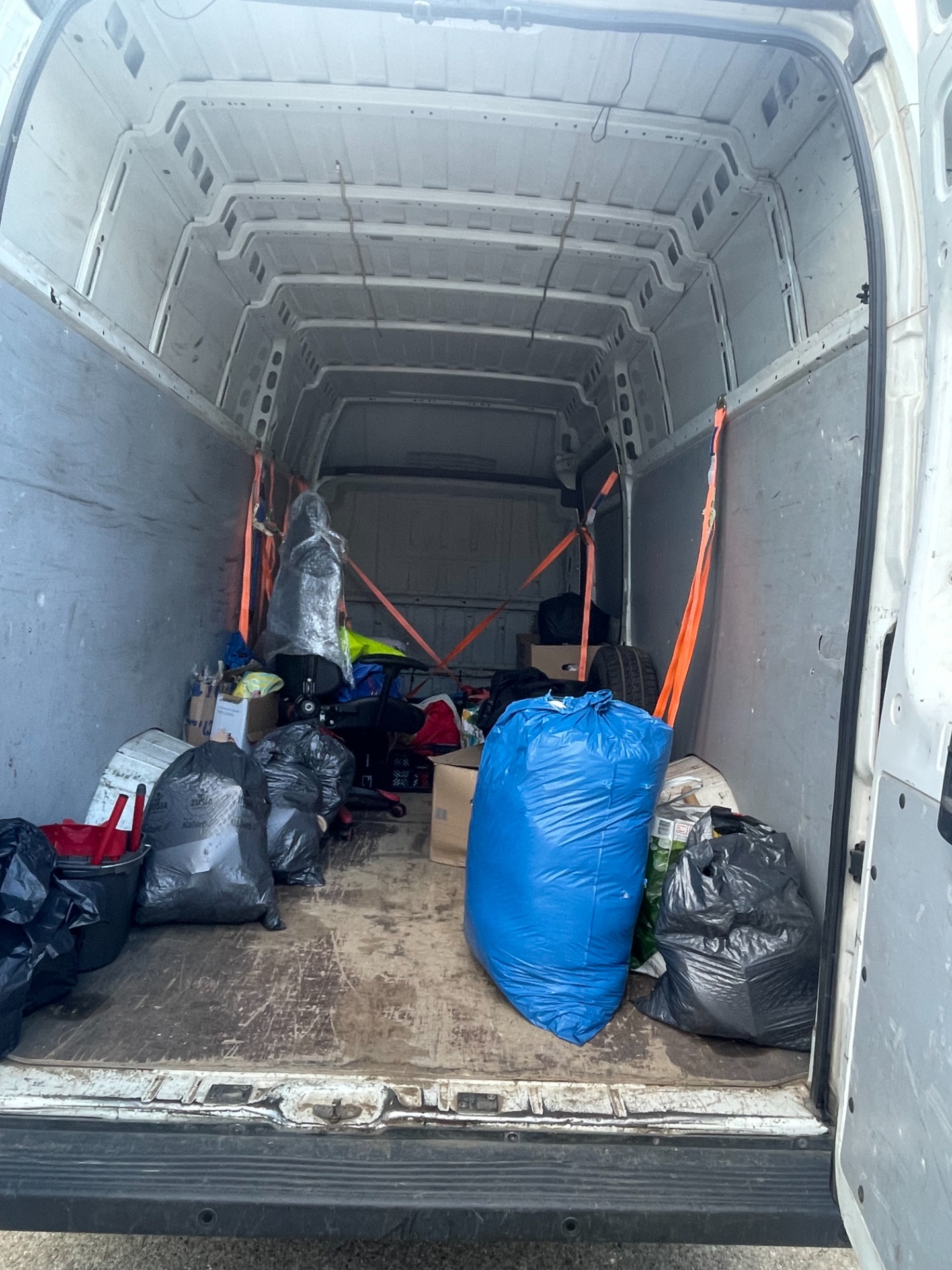 Worki z rzeczami i zabezpieczony fotel obrotowy przygotowane do transportu bagażowego na pace busa Mrówka Trans.